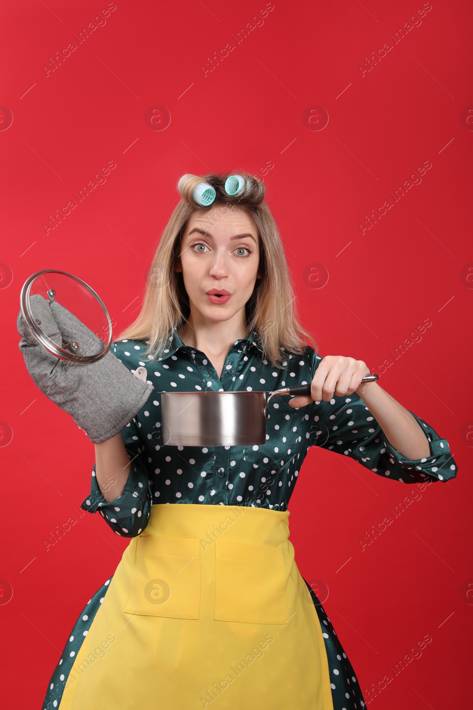 Young housewife with saucepan on red background Photo of Young housewife with saucepan on red background