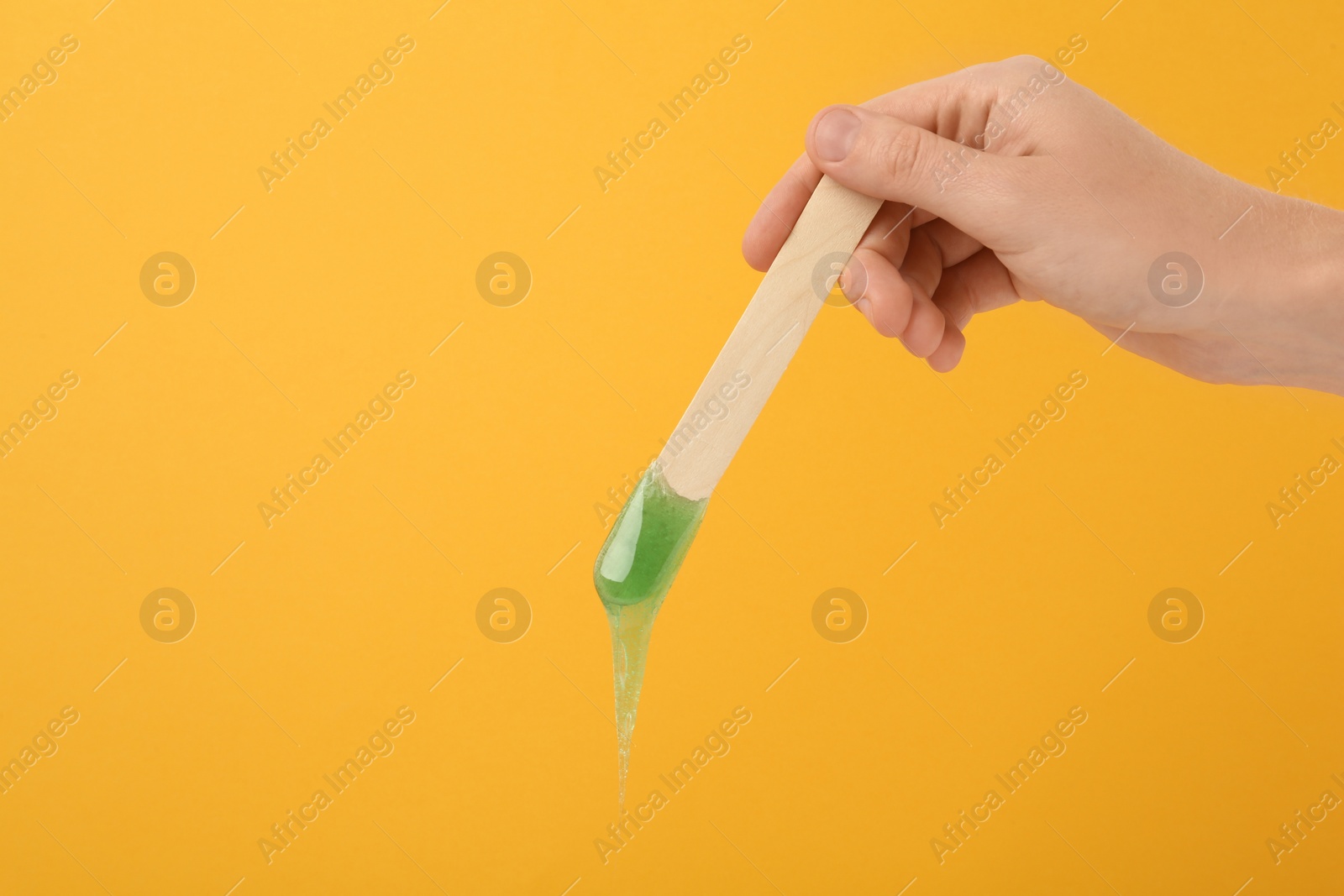 Woman holding spatula with hot depilatory wax on yellow background, closeup. Space for text Photo of Woman holding spatula with hot depilatory wax on yellow background, closeup. Space for text