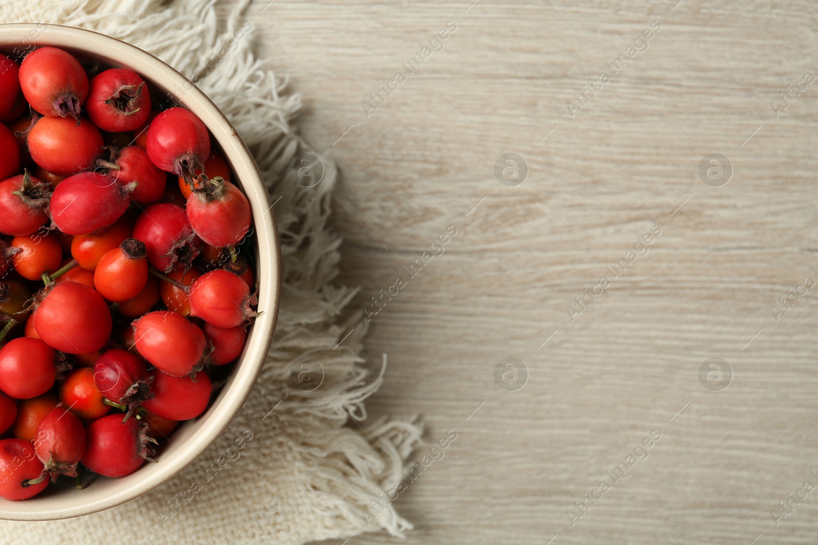 Ripe rose hip berries in bowl on wooden table, top view. Space for text Photo of Ripe rose hip berries in bowl on wooden table, top view. Space for text