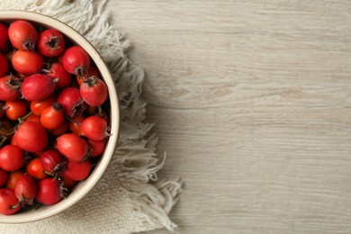 Ripe rose hip berries in bowl on wooden table, top view. Space for text Photo of Ripe rose hip berries in bowl on wooden table, top view. Space for text