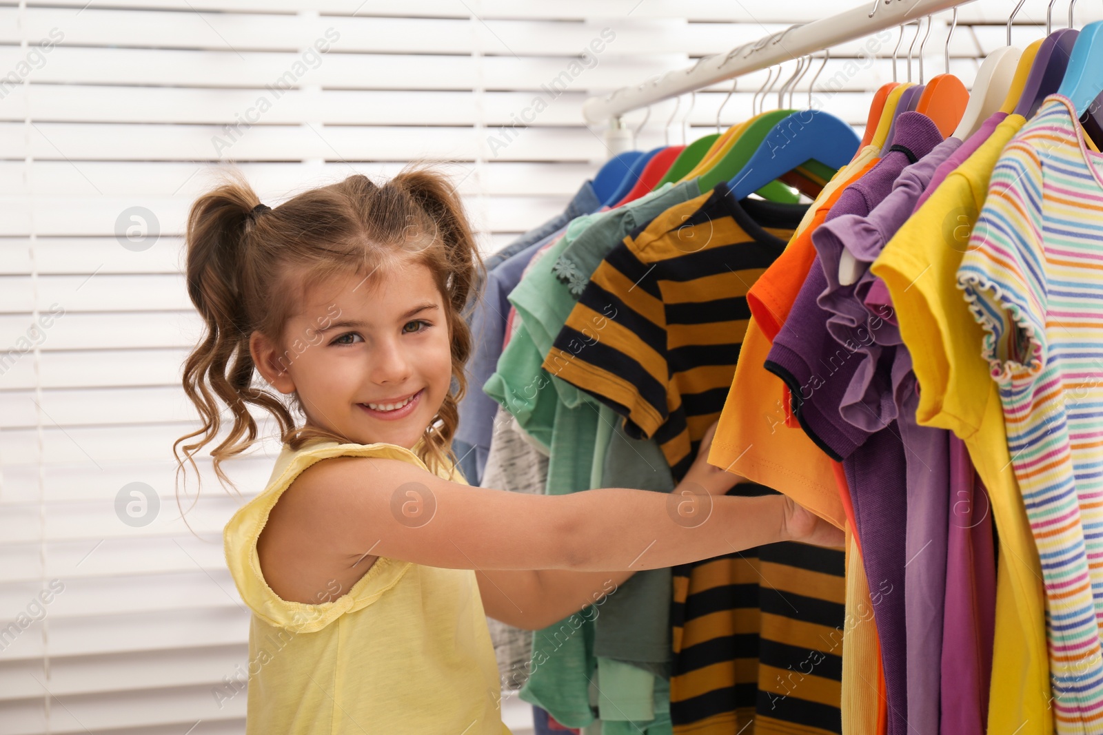 Little girl choosing clothes on rack indoors Photo of Little girl choosing clothes on rack indoors