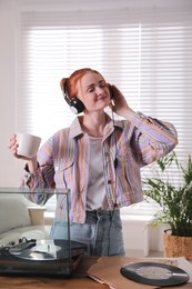 Young woman drinking coffee while listening to music with turntable at home Photo of Young woman drinking coffee while listening to music with turntable at home