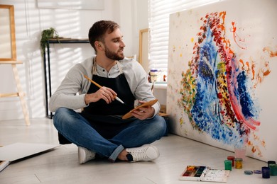 Young man painting on canvas with brush in artist studio Photo of Young man painting on canvas with brush in artist studio