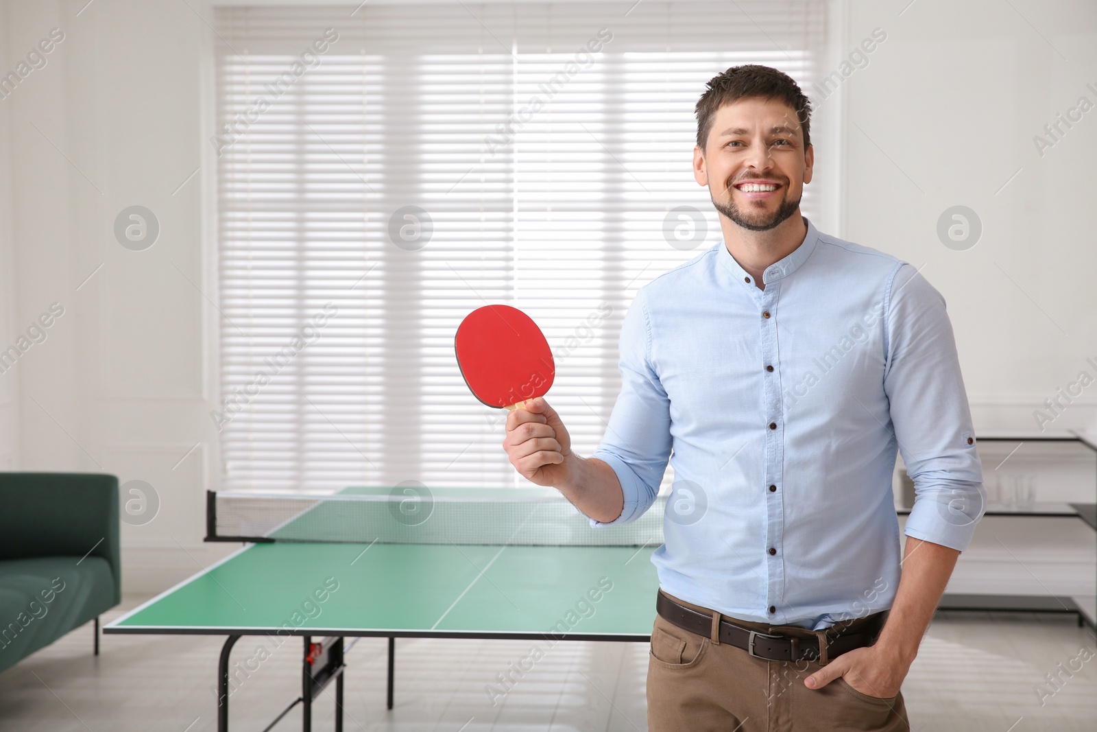 Businessman with tennis racket near ping pong table in office. Space for text Photo of Businessman with tennis racket near ping pong table in office. Space for text