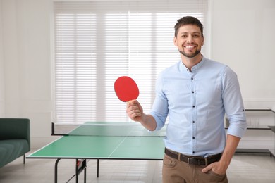 Businessman with tennis racket near ping pong table in office. Space for text Photo of Businessman with tennis racket near ping pong table in office. Space for text