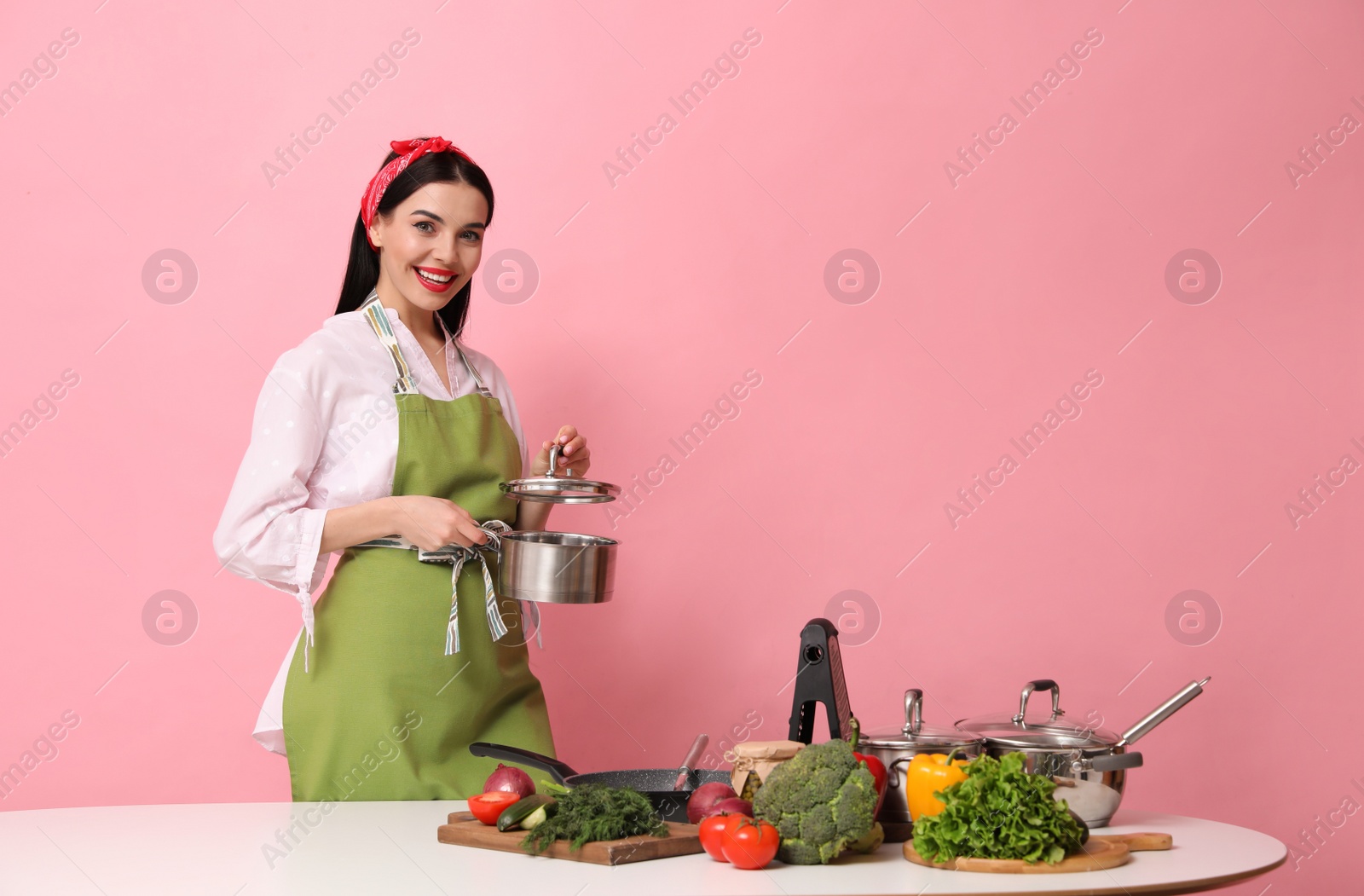Young housewife with vegetables and different utensils on pink background. Space for text Photo of Young housewife with vegetables and different utensils on pink background. Space for text