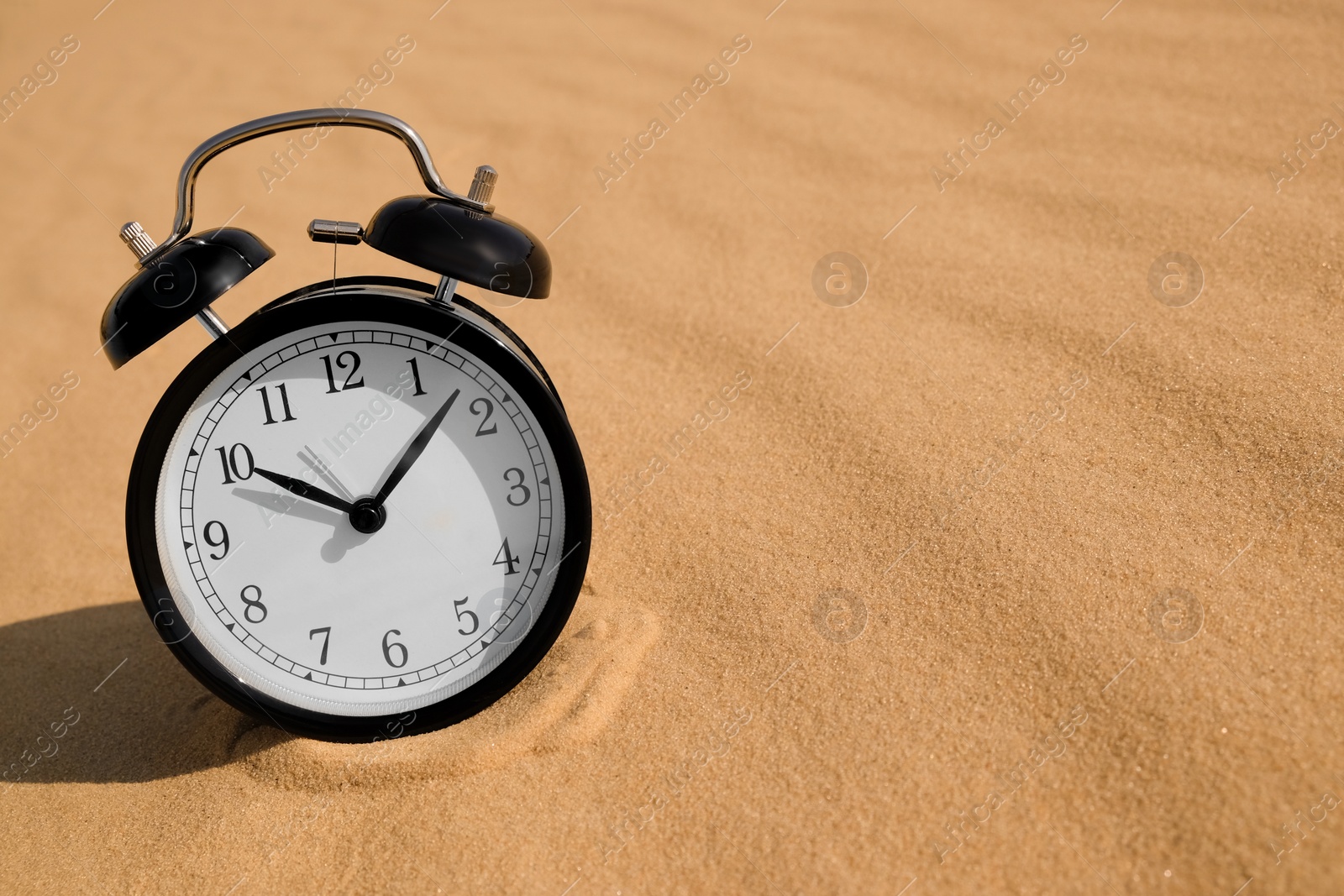 Black alarm clock on sand in desert. Space for text Photo of Black alarm clock on sand in desert. Space for text