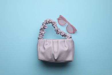 Stylish woman's bag and sunglasses on light blue background, flat lay Photo of Stylish woman's bag and sunglasses on light blue background, flat lay