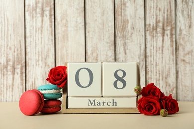 Wooden block calendar with date 8th of March, macarons and roses on table against light background, space for text. International Women's Day Photo of Wooden block calendar with date 8th of March, macarons and roses on table against light background, space for text. International Women's Day