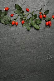 Ripe rose hip berries with green leaves on black table, flat lay. Space for text Photo of Ripe rose hip berries with green leaves on black table, flat lay. Space for text