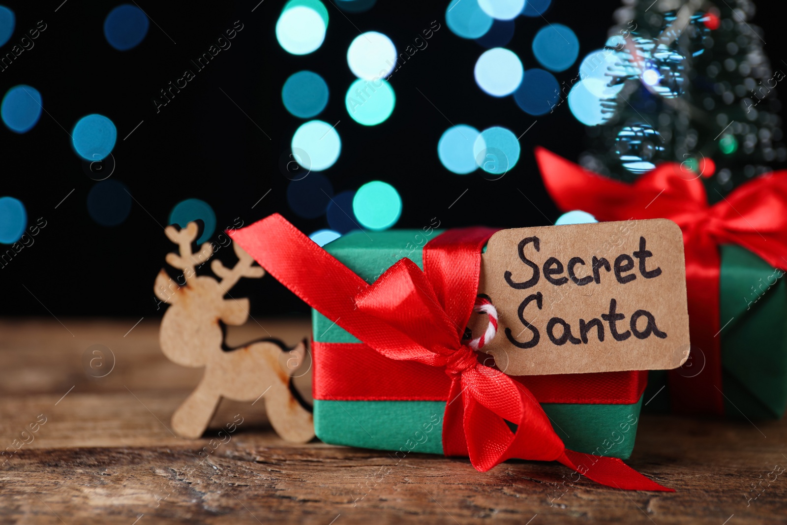Present from secret Santa on wooden table against blurred lights Photo of Present from secret Santa on wooden table against blurred lights