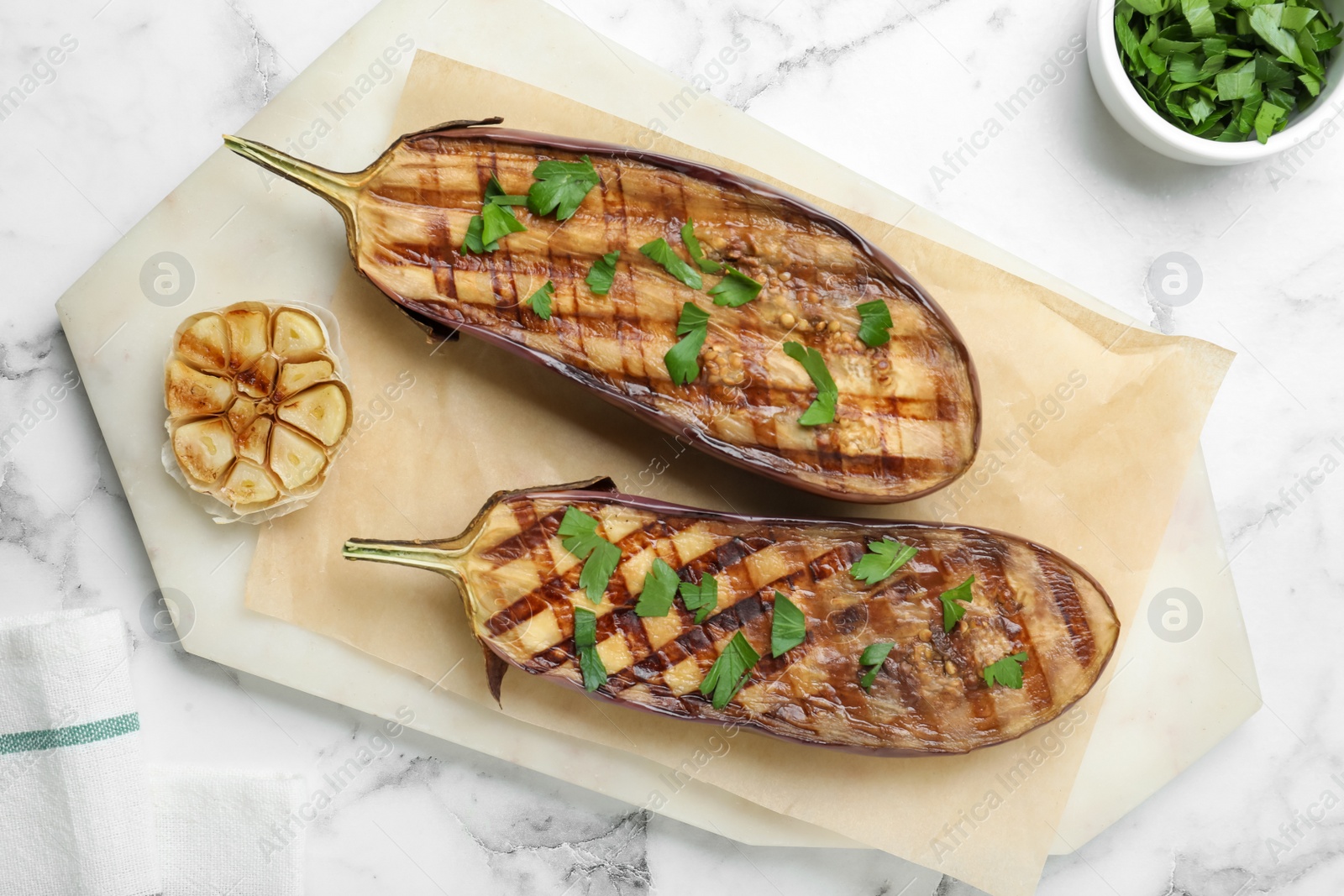 Delicious grilled eggplant halves with parsley on white marble table, flat lay Photo of Delicious grilled eggplant halves with parsley on white marble table, flat lay