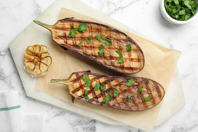 Delicious grilled eggplant halves with parsley on white marble table, flat lay Photo of Delicious grilled eggplant halves with parsley on white marble table, flat lay