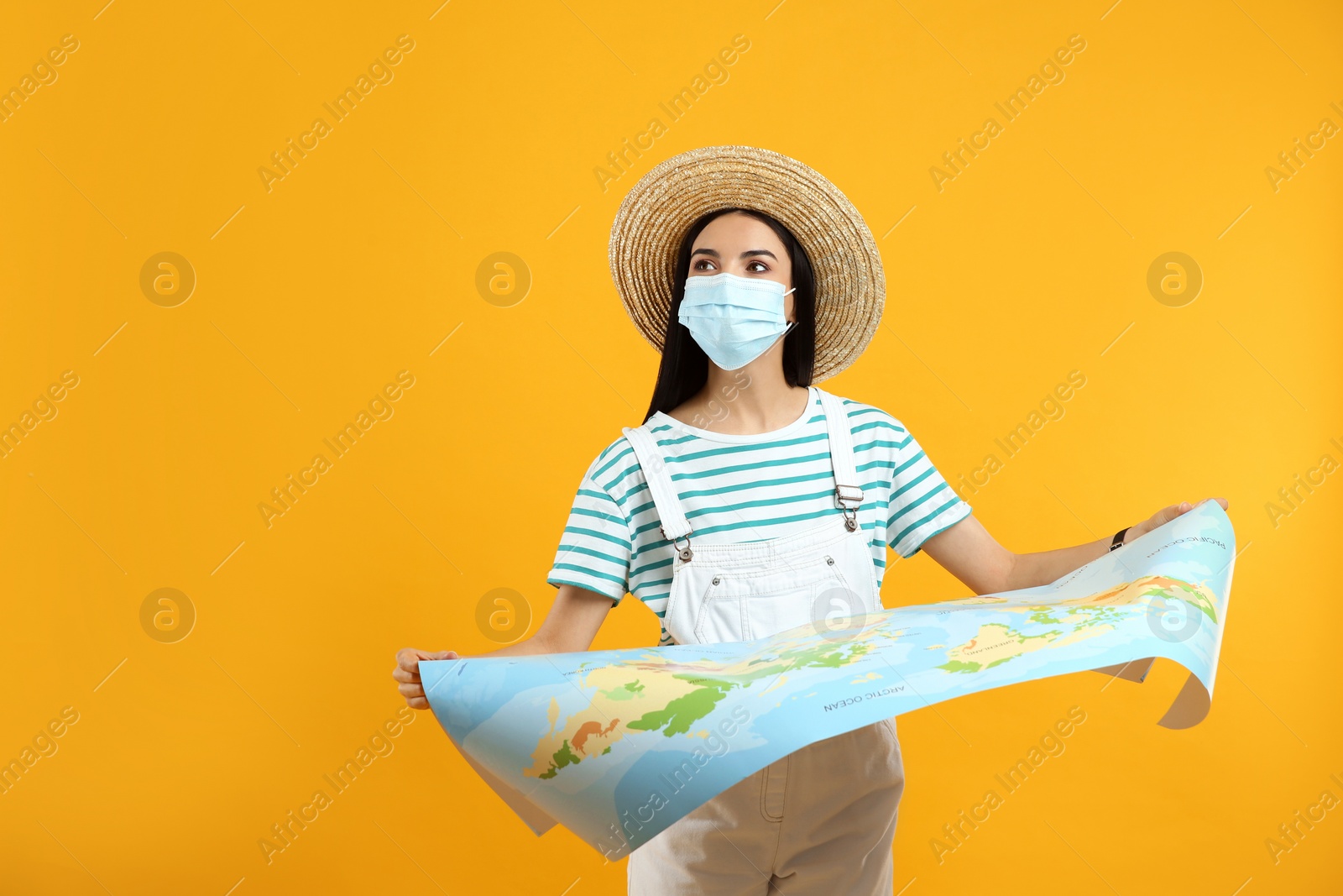 Female tourist in medical mask with map on yellow background, space for text. Travelling during coronavirus pandemic Photo of Female tourist in medical mask with map on yellow background, space for text. Travelling during coronavirus pandemic