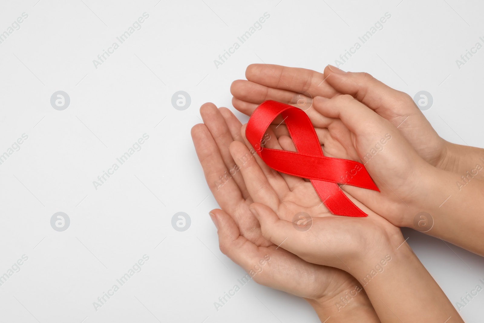 Woman and girl holding red ribbon on white background, top view with space for text. AIDS disease awareness Photo of Woman and girl holding red ribbon on white background, top view with space for text. AIDS disease awareness