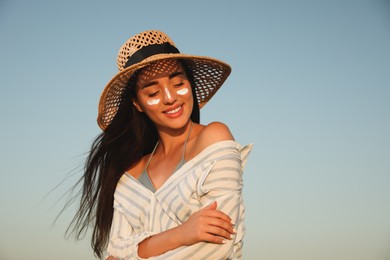 Happy young woman with sun protection cream on face against blue sky Photo of Happy young woman with sun protection cream on face against blue sky