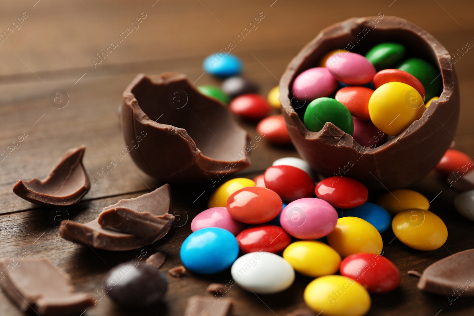 Broken chocolate egg and colorful candies on wooden table, closeup Photo of Broken chocolate egg and colorful candies on wooden table, closeup
