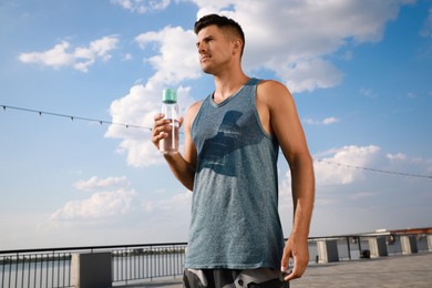 Handsome man in sportswear with bottle of water outdoors on sunny day Photo of Handsome man in sportswear with bottle of water outdoors on sunny day