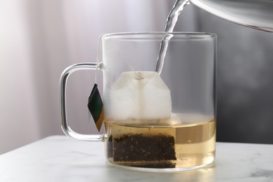 Pouring hot water into glass cup with tea bag on table Photo of Pouring hot water into glass cup with tea bag on table