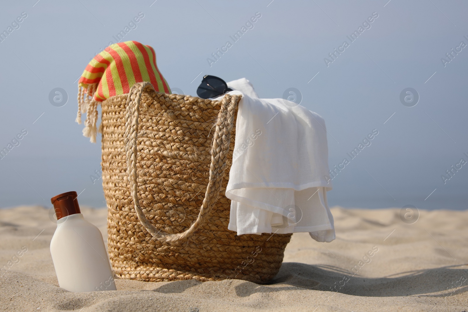 Beach bag, towel, blanket, sunglasses and sunscreen on sandy seashore, space for text Photo of Beach bag, towel, blanket, sunglasses and sunscreen on sandy seashore, space for text