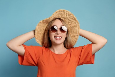 Beautiful young woman wearing straw hat and sunglasses on light blue background. Stylish headdress Photo of Beautiful young woman wearing straw hat and sunglasses on light blue background. Stylish headdress