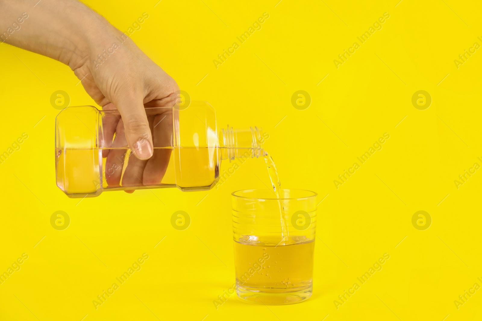 Woman pouring mouthwash into glass on yellow background, closeup Photo of Woman pouring mouthwash into glass on yellow background, closeup