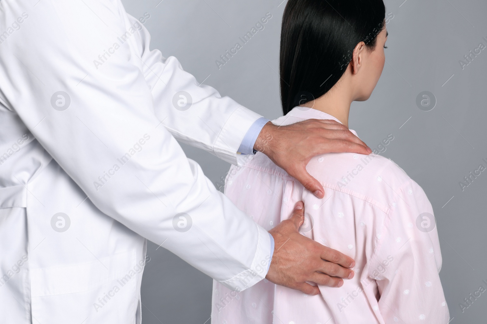 Doctor examining woman with shoulder pain on grey background Photo of Doctor examining woman with shoulder pain on grey background