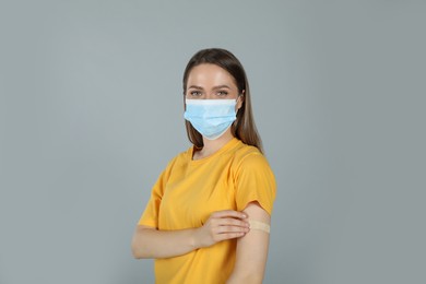 Vaccinated woman with protective mask and medical plaster on her arm against grey background Photo of Vaccinated woman with protective mask and medical plaster on her arm against grey background