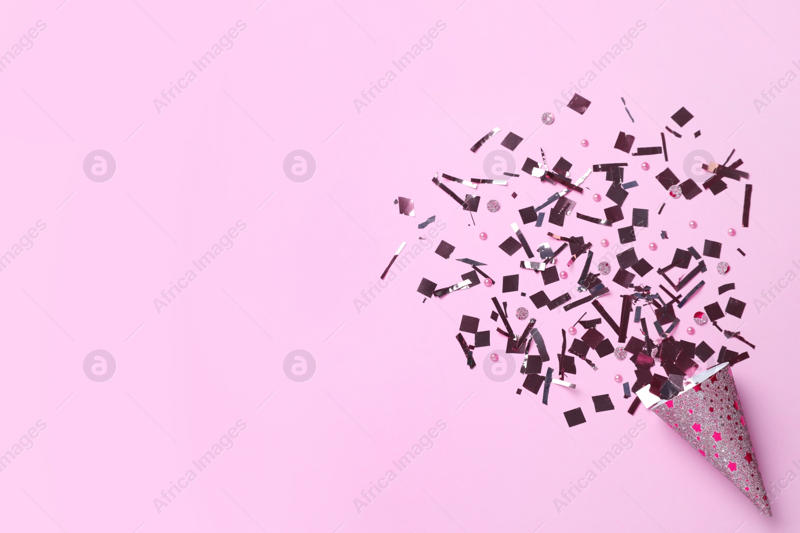 Shiny silver confetti bursting out of party cracker on pink background, top view. Space for text Photo of Shiny silver confetti bursting out of party cracker on pink background, top view. Space for text