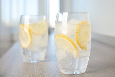 Soda water with lemon slices and ice cubes on wooden table indoors. Space for text Photo of Soda water with lemon slices and ice cubes on wooden table indoors. Space for text