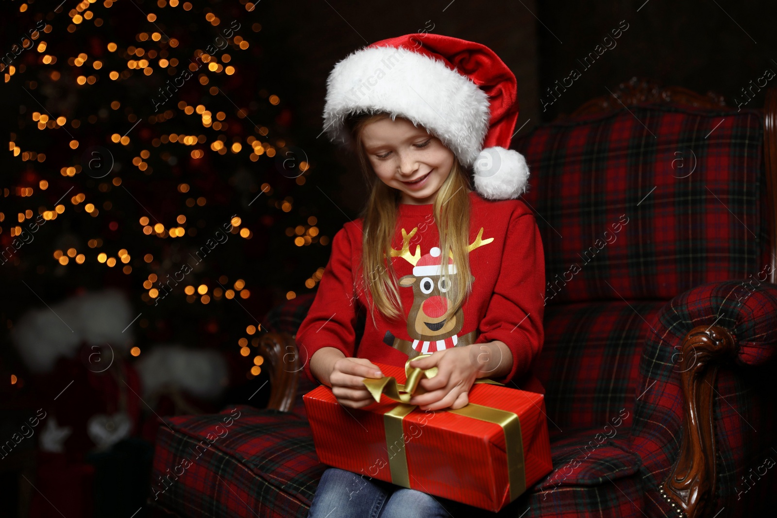 Cute little child with Christmas gift sitting in armchair at home Photo of Cute little child with Christmas gift sitting in armchair at home