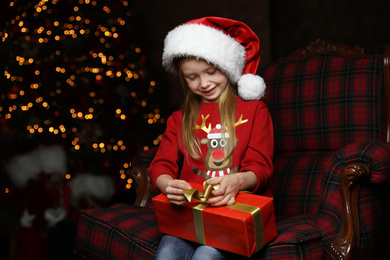 Cute little child with Christmas gift sitting in armchair at home Photo of Cute little child with Christmas gift sitting in armchair at home