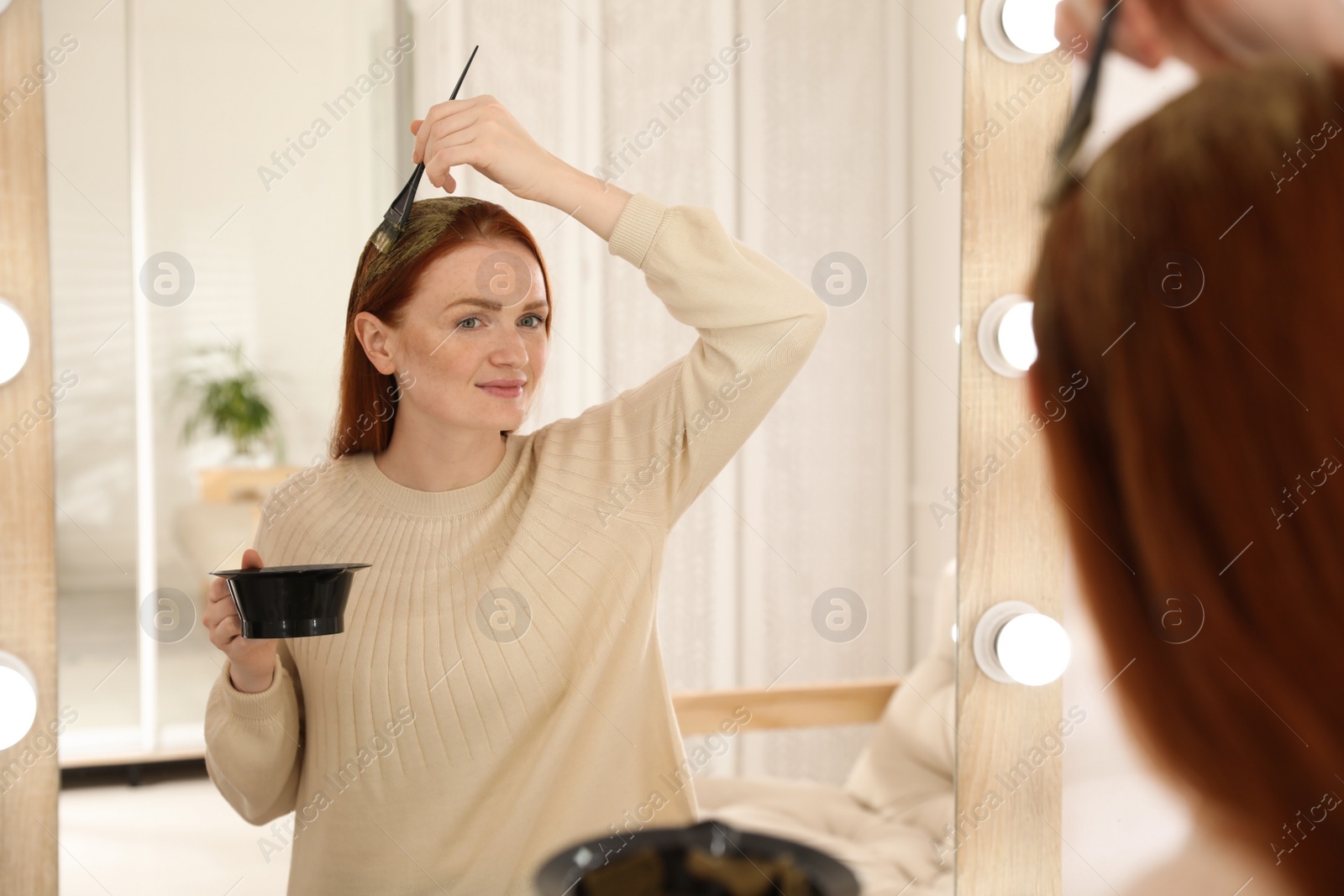 Young woman dyeing her hair with henna near mirror Photo of Young woman dyeing her hair with henna near mirror