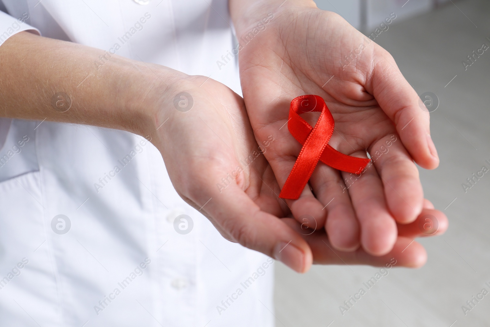 Doctor holding red awareness ribbon indoors, closeup. World AIDS disease day Photo of Doctor holding red awareness ribbon indoors, closeup. World AIDS disease day