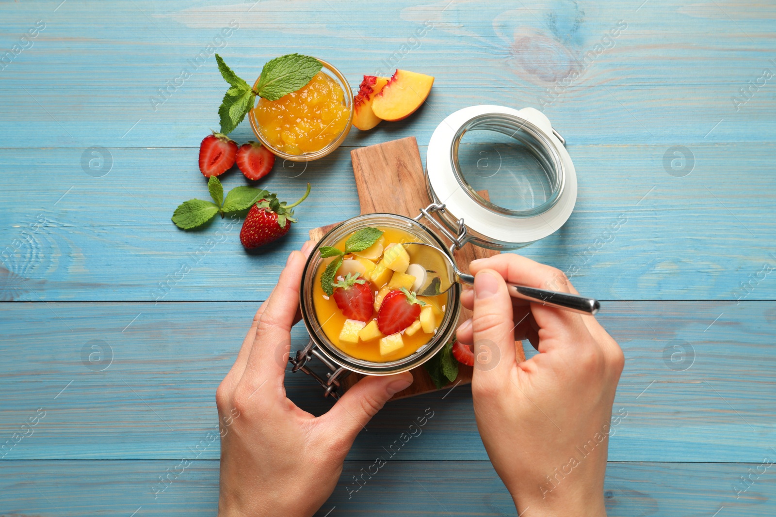 Woman eating delicious mango jelly with fresh fruits at light blue wooden table, top view Photo of Woman eating delicious mango jelly with fresh fruits at light blue wooden table, top view