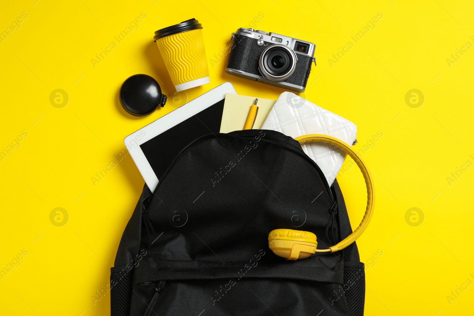 Stylish urban backpack with different items on yellow background, flat lay Photo of Stylish urban backpack with different items on yellow background, flat lay