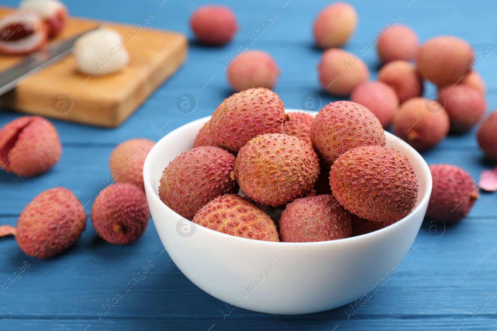 Photo of Fresh ripe lychee fruits in bowl on blue wooden table