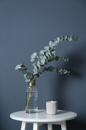 Beautiful eucalyptus branches and burning candle on white table near blue wall. Interior element Photo of Beautiful eucalyptus branches and burning candle on white table near blue wall. Interior element