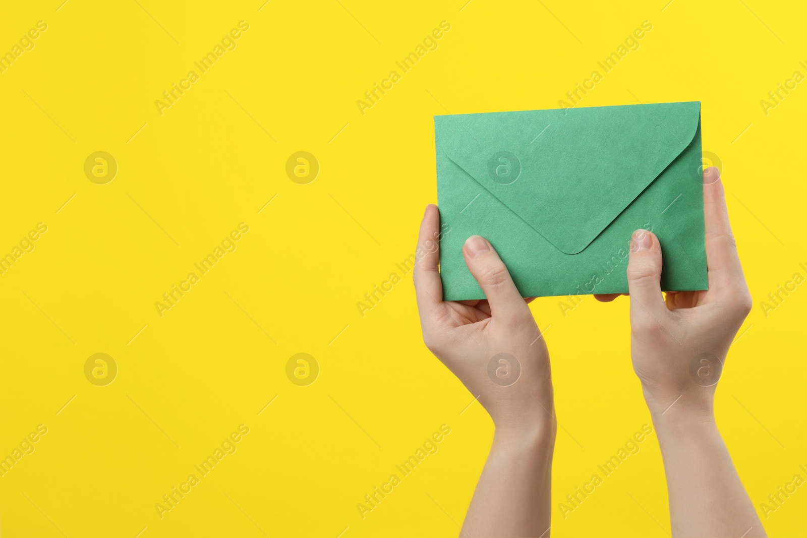 Woman holding green paper envelope on yellow background, closeup. Space for text Photo of Woman holding green paper envelope on yellow background, closeup. Space for text