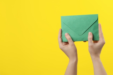 Woman holding green paper envelope on yellow background, closeup. Space for text Photo of Woman holding green paper envelope on yellow background, closeup. Space for text
