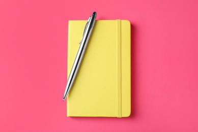 New stylish planner with hard cover and pen on pink background, top view Photo of New stylish planner with hard cover and pen on pink background, top view