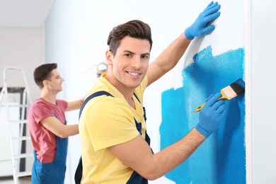 Photo of Male decorator painting wall with brush indoors