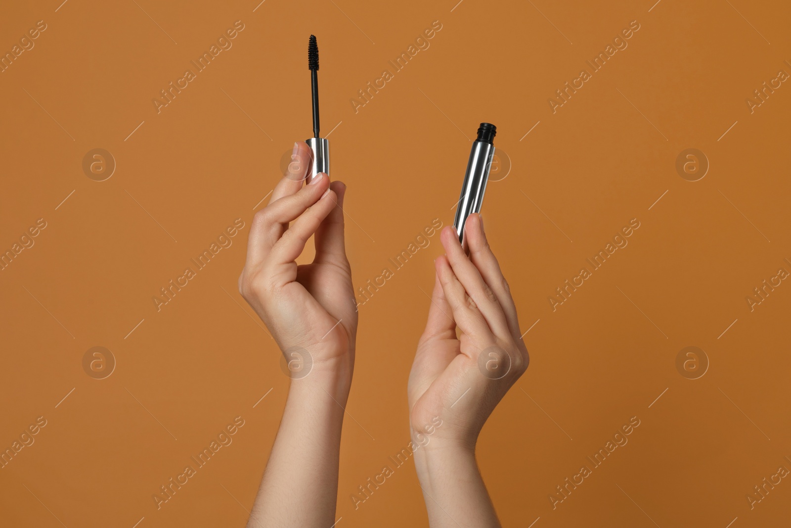 Photo of Woman holding mascara for eyelashes on light brown background, closeup