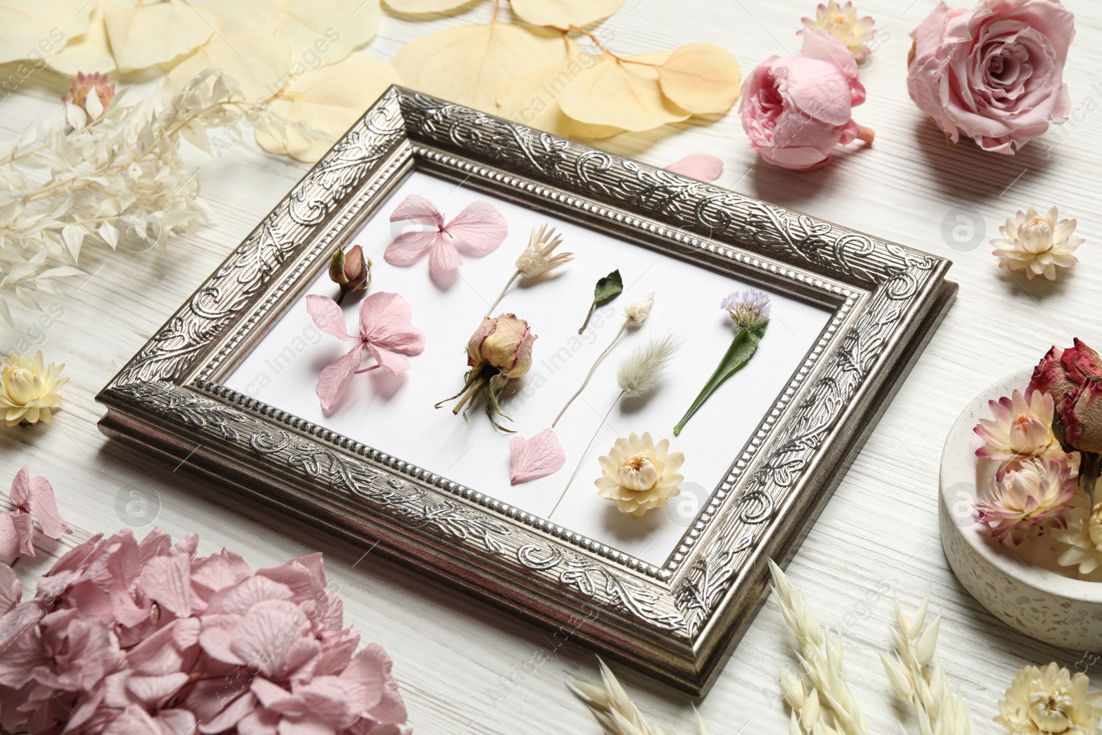 Composition with beautiful dry flowers and vintage frame on white wooden background Photo of Composition with beautiful dry flowers and vintage frame on white wooden background