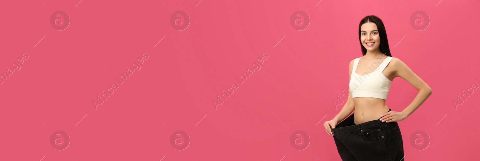 Happy young woman wearing big jeans after weight loss on pink background Photo of Happy young woman wearing big jeans after weight loss on pink background
