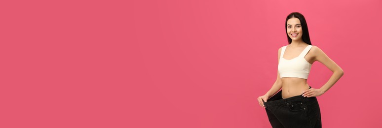 Happy young woman wearing big jeans after weight loss on pink background Photo of Happy young woman wearing big jeans after weight loss on pink background