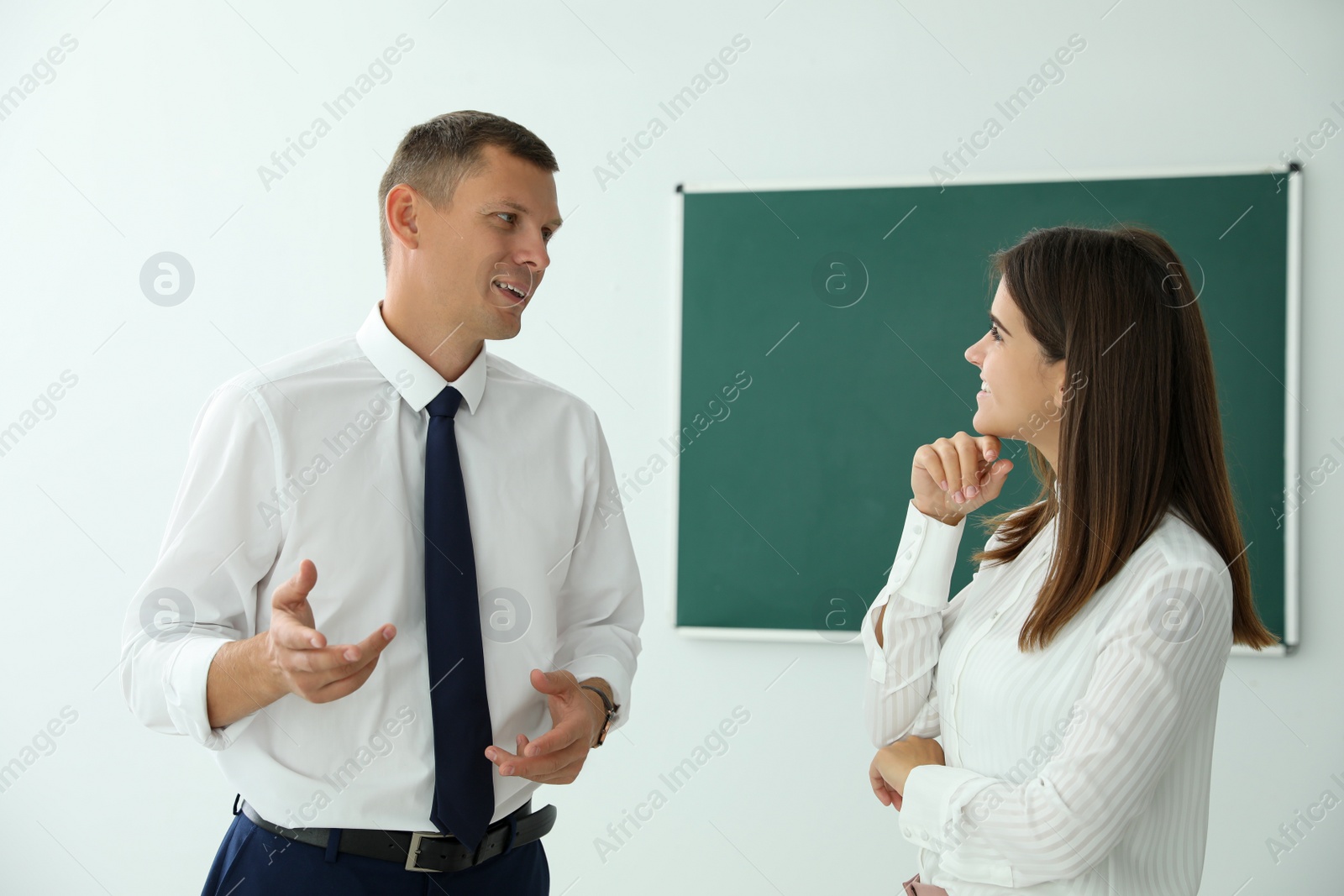 Photo of Man and woman talking near green chalkboard in classroom