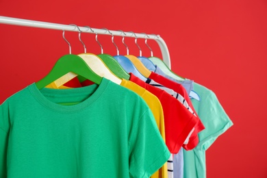 Rack with stylish children clothes on red background, closeup Photo of Rack with stylish children clothes on red background, closeup
