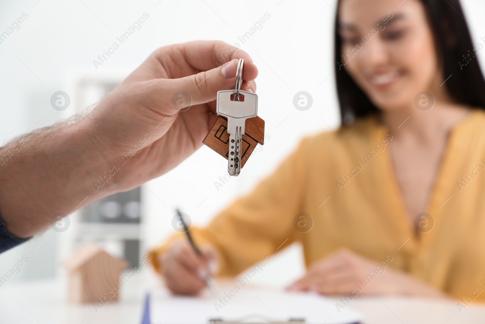 Happy young woman signing purchase contract in office. Real estate agent holding new house key, closeup Photo of Happy young woman signing purchase contract in office. Real estate agent holding new house key, closeup