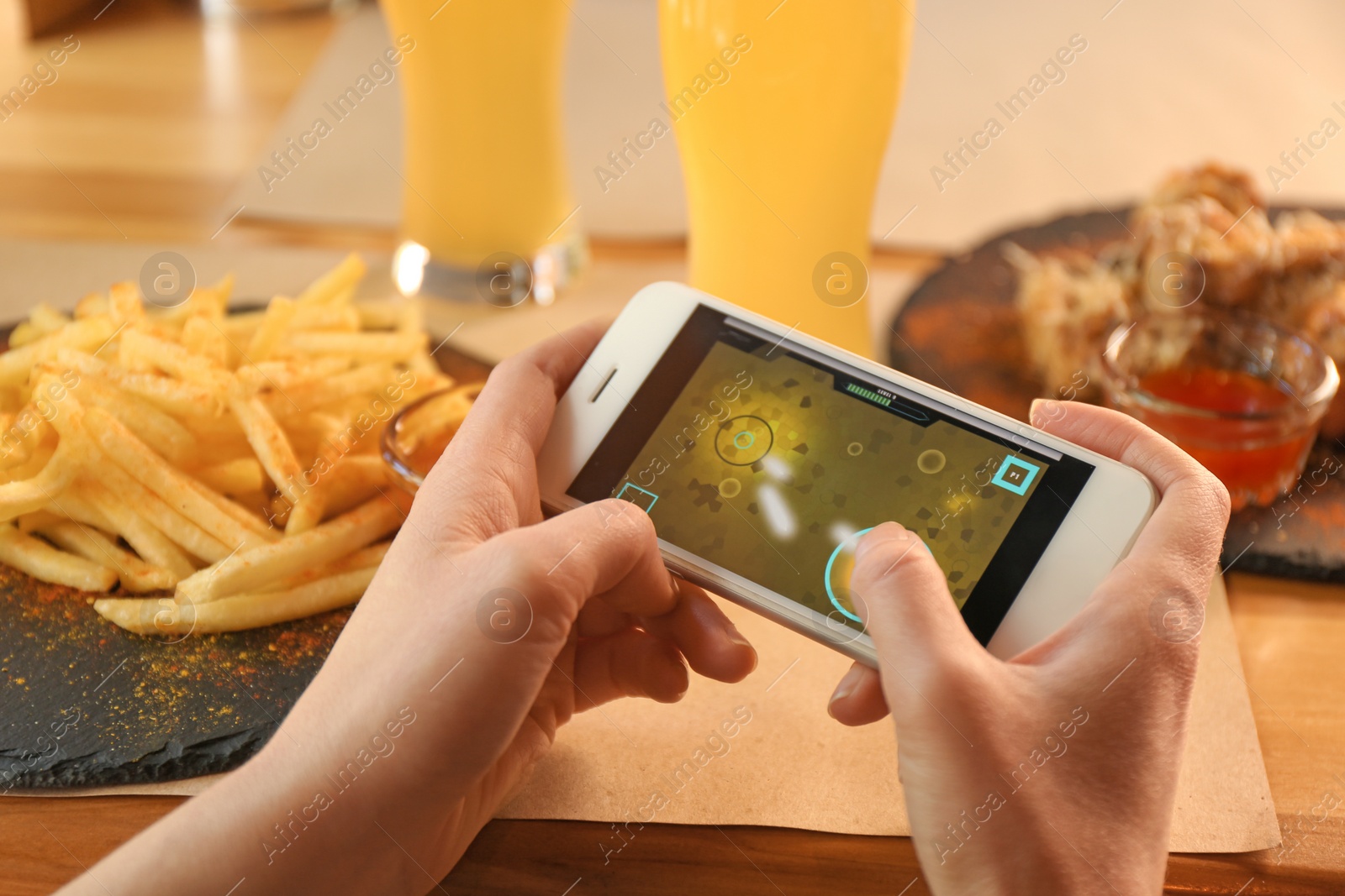 Woman playing game using smartphone at table with tasty snacks, closeup Photo of Woman playing game using smartphone at table with tasty snacks, closeup